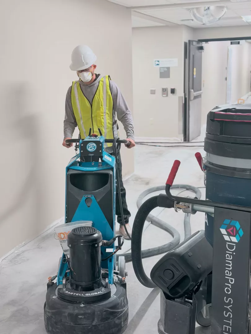 Worker preparing an indoor concrete floor with grinding and dust collection equipment